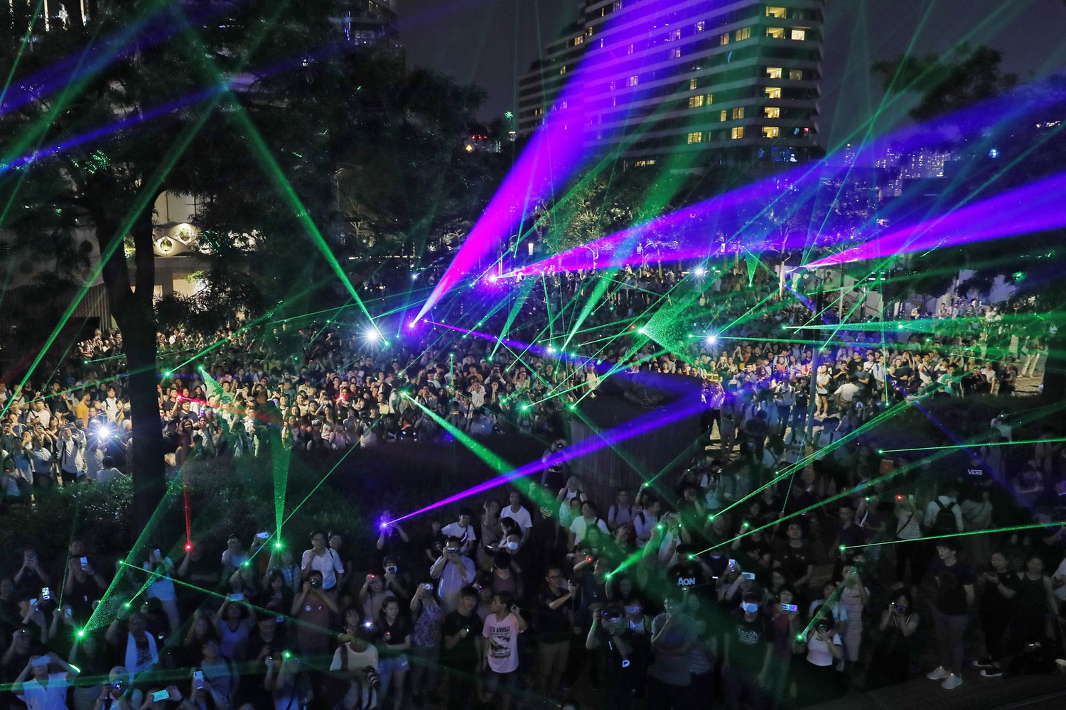 Photograph of green and fuschia laser beams being pointed from a crowd of protestors.